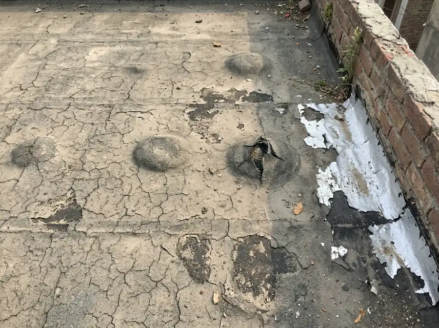 Blisters, cracks and peeling coating on an old flat roof by a brick parapet