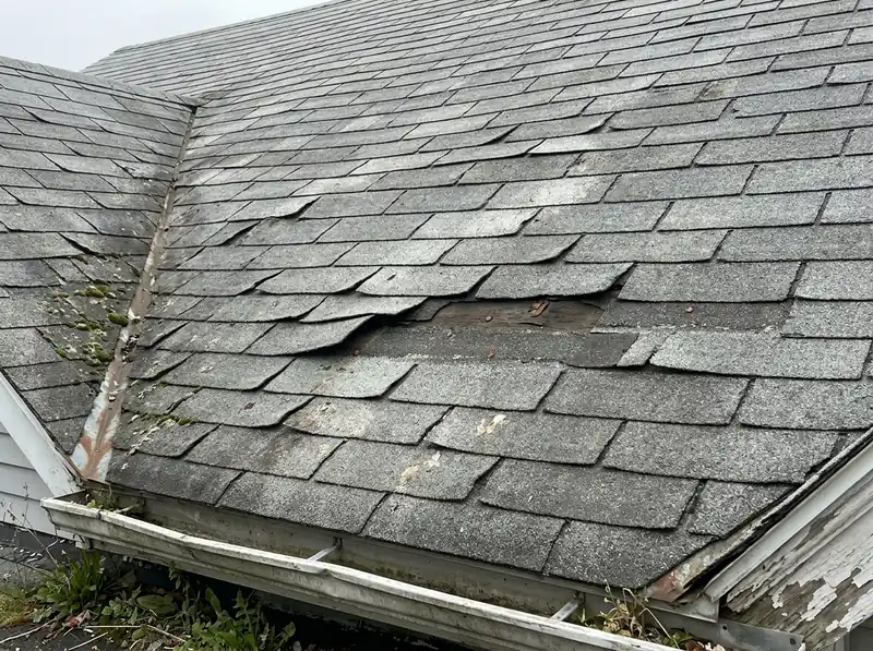 Curled and lifting asphalt shingles near a roof valley on an older house