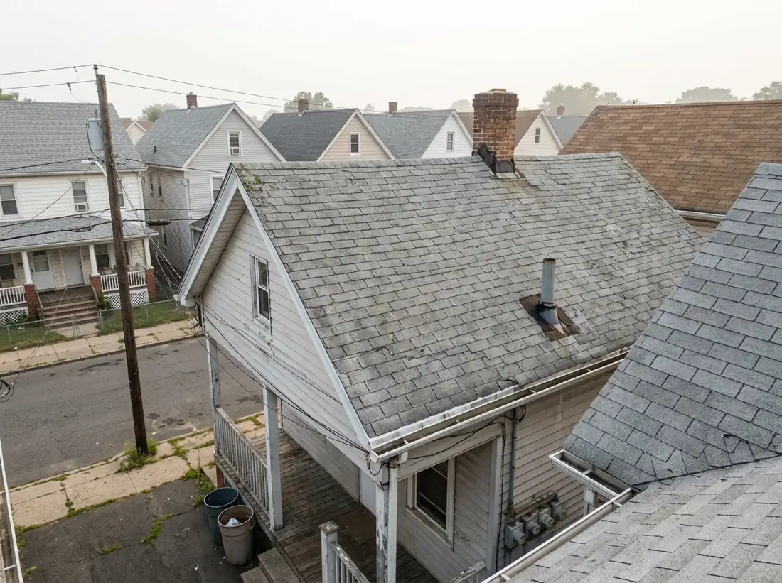 Weathered gray asphalt shingle roof with a brick chimney and vent pipe on a two-family home