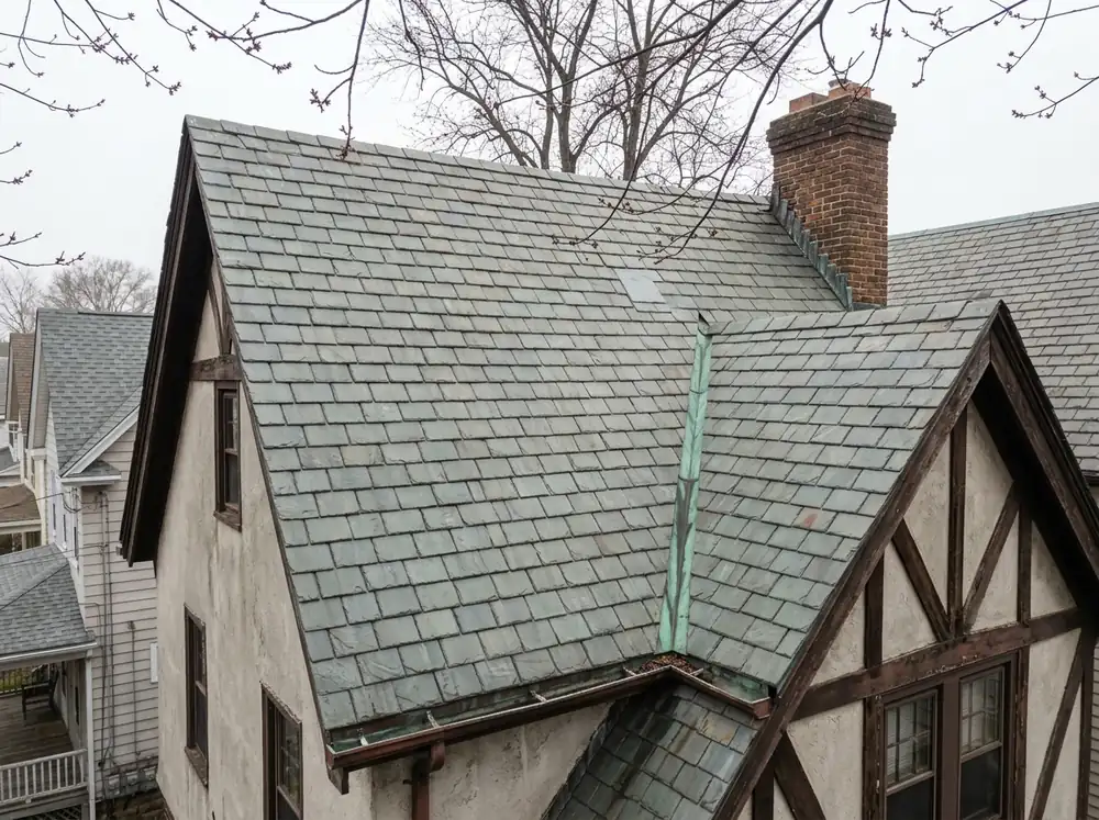 Gray-green slate roof with copper valley flashing and a brick chimney on a Tudor-style home